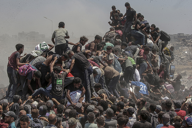 Palestinians climb onto an aid truck as it enters the Gaza Strip by Saber Nuraldin _ © Saber Nuraldin, EPA Images. Title: Aid Emergency in Gaza Credit: © Saber Nuraldin, EPA ImagesCaption: Palestinians climb onto an aid truck as it enters the Gaza Strip via the Zikim Crossing in an attempt to get flour, during what the Israeli military called a “tactical suspension” in operations to allow humanitarian aid through. 27 July 2025.Story: In 2025, famine took hold amid what an independent UN Human Rights Commission inquiry has concluded is a genocide in Gaza. Israel disputes this. Israeli authorities imposed a complete aid blockade in March, a tactic described by humanitarian organizations as the weaponization of starvation. When international pressure led to a partial reopening of crossings in May, most deliveries went through the Gaza Humanitarian Foundation (GHF), established by the US and Israel to bypass the UN-led aid system. Its operation, which put military personnel in charge, was widely condemned by global human rights and legal organizations as unethical and in violation of international law. The UN reports that between late May and early October, at least 2,435 Palestinians were killed seeking food at or near GHF collection points. The GHF shut down when a fragile ceasefire went into effect in October. Despite some aid entering Gaza, more than 75% of the population still faced hunger and malnutrition in December. The photographer was born in Gaza and has documented life there since 1997.
